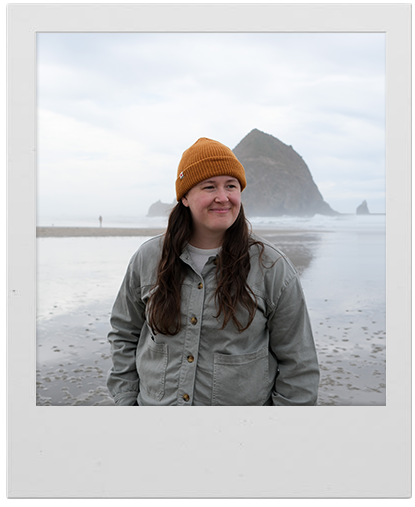 Polaroid of Alex at Cannon Beach, Oregon, in a mustard beanie with Haystack Rock behind her